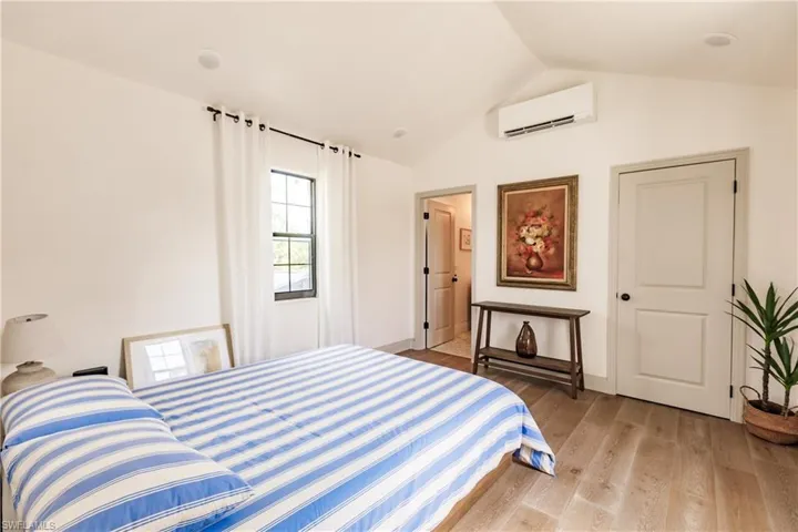 Bedroom featuring lofted ceiling, light hardwood / wood-style flooring, and a wall mounted air conditioner