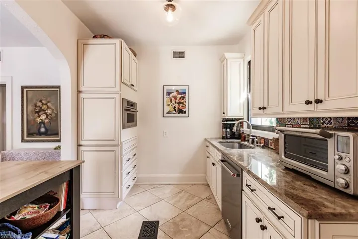 Kitchen with cream cabinets, sink, stainless steel appliances, dark stone countertops, and light tile patterned floors