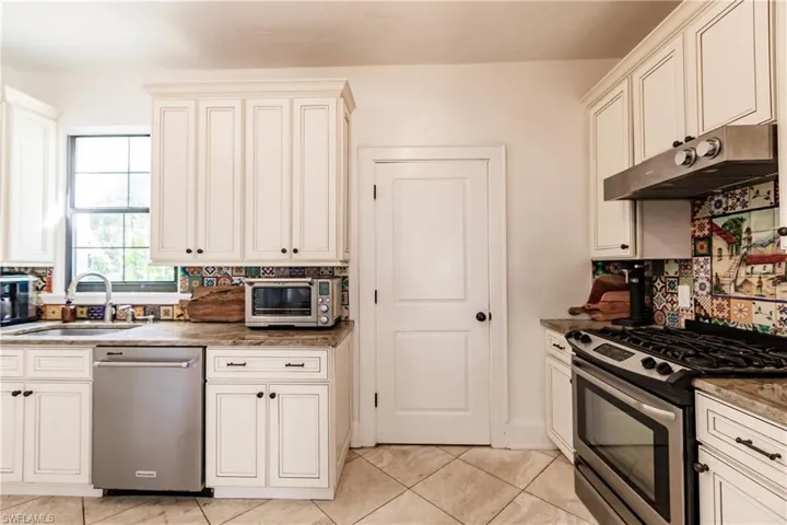 Kitchen with decorative backsplash, light tile patterned floors, dark stone countertops, sink, and stainless steel appliances