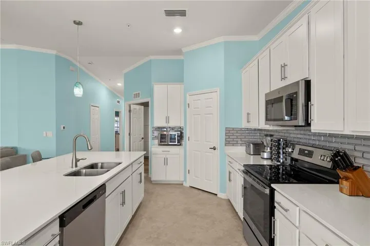 Kitchen featuring appliances with stainless steel finishes, a sink, ornamental molding, tasteful backsplash, and light countertops