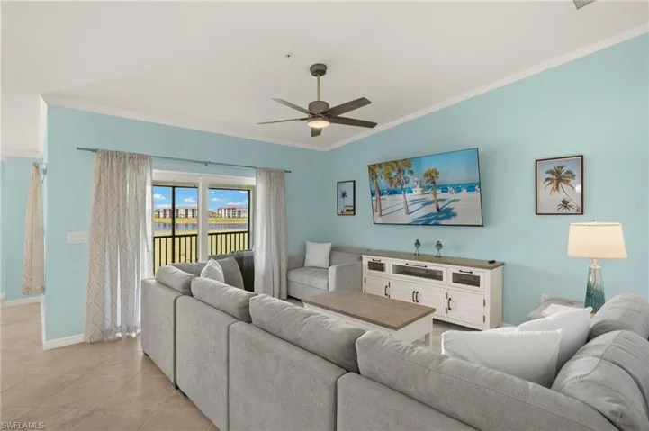 Living room with crown molding, ceiling fan, baseboards, light tile patterned flooring, and vaulted ceiling