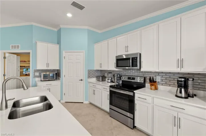 Kitchen featuring appliances with stainless steel finishes, a sink, white cabinets, light countertops, and decorative backsplash