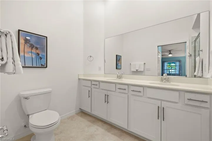 Full bathroom featuring double vanity, toilet, baseboards, a shower with door, and tile patterned floors