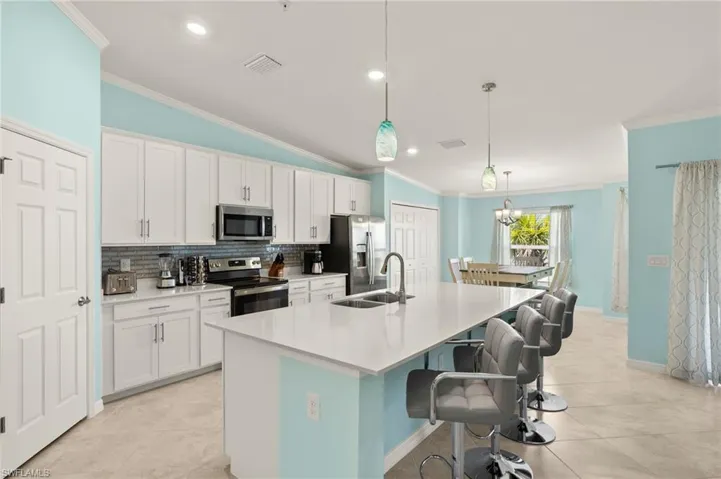 Kitchen with stainless steel appliances, a sink, crown molding, tasteful backsplash, and a center island with sink