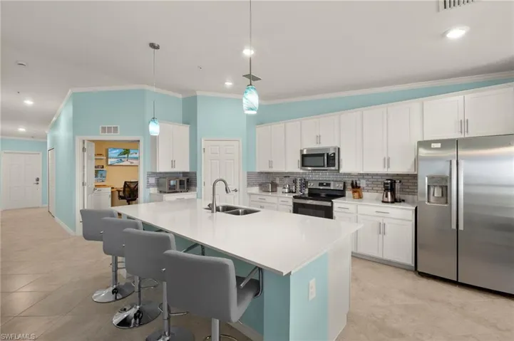 Kitchen featuring appliances with stainless steel finishes, a sink, crown molding, backsplash, and a kitchen bar