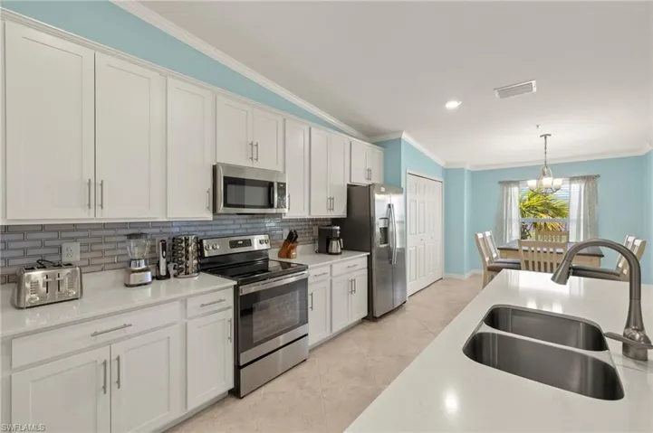 Kitchen featuring stainless steel appliances, a sink, ornamental molding, decorative backsplash, and vaulted ceiling