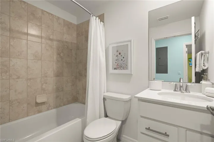 Bathroom with shower / bath combination with curtain, toilet, vanity, and electric panel