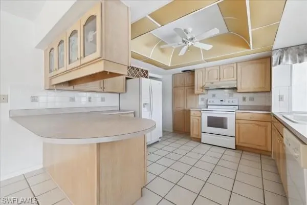 Kitchen with light tile patterned flooring, ceiling fan, tasteful backsplash, a tray ceiling, and white appliances