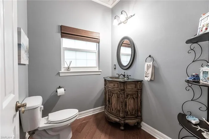 Half Bathroom with hardwood / wood-style floors, ornamental molding, vanity, and toilet