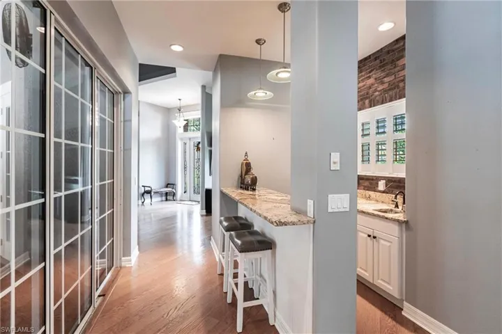 Bar with hardwood / wood-style floors, sink, pendant lighting, and light stone countertops