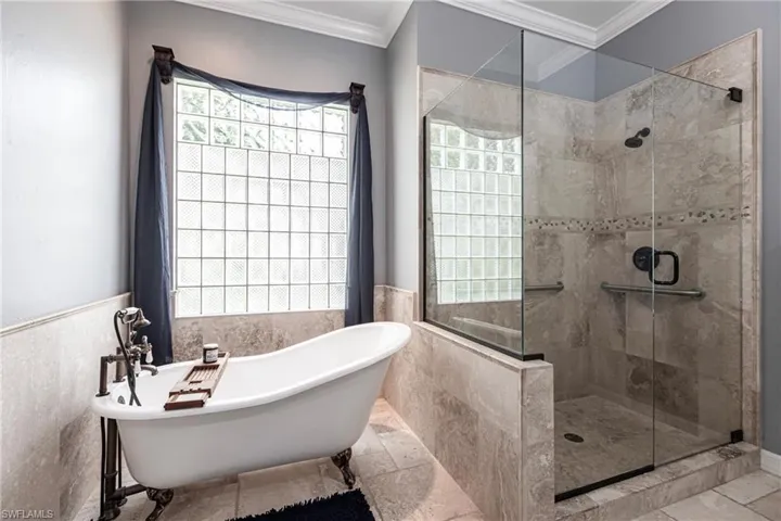 Bathroom with tile patterned floors, tile walls, separate shower and tub, and crown molding