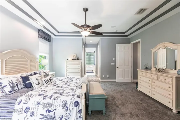 Bedroom featuring dark colored carpet, ceiling fan, and a tray ceiling