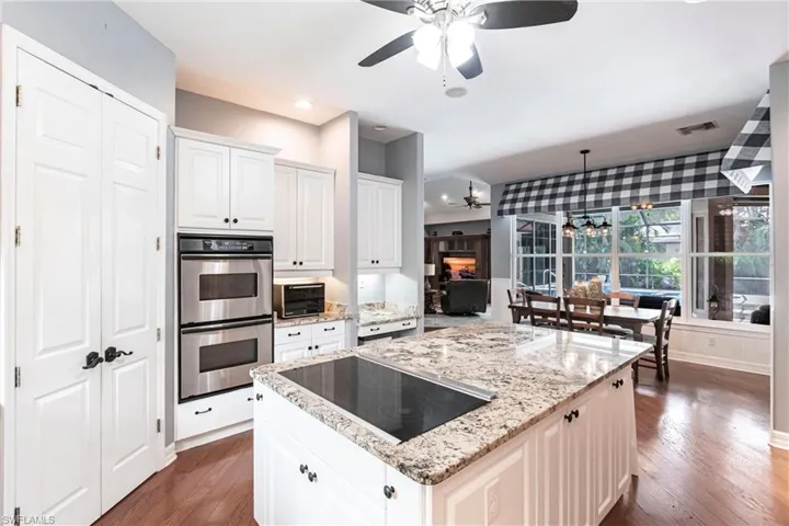 Kitchen with stainless steel double oven, light stone countertops, black electric cooktop, ceiling fan, and dark hardwood / wood-style floors