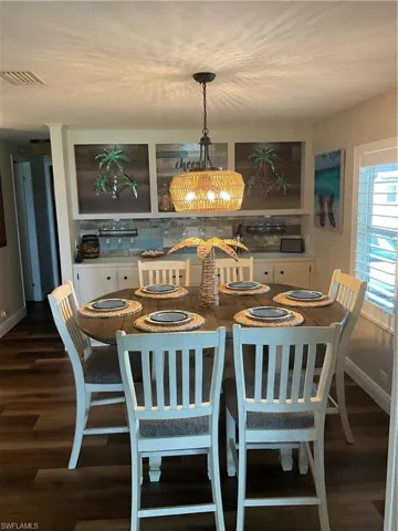 Dining area featuring wood-finish flooring, a woven pendant light fixture, and built-in cabinetry with glass shelving