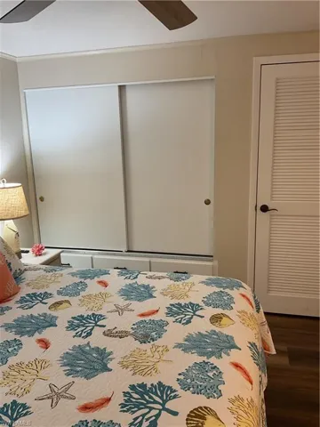 Bedroom featuring sliding closet doors, a louvered door, wood-finish flooring, and a ceiling fan