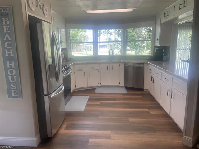 Kitchen featuring wood-finish flooring, white cabinetry with dark hardware, a stainless steel refrigerator, and ample counter space with a light-colored surface