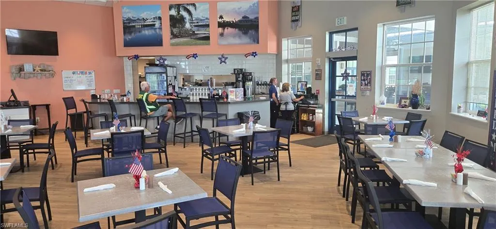 Spacious dining area featuring wood-finish flooring, a long bar with seating, multiple dining tables, large windows, and recessed lighting