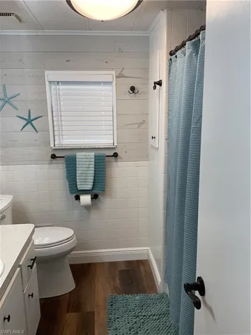 Bathroom featuring wood-finish flooring, white tile wainscoting, and shiplap-style wall paneling