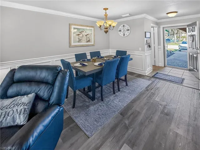 Dining space featuring wainscoting, ornamental molding, wood finished floors, a decorative wall, and hanging lights