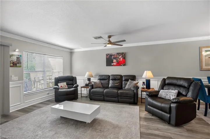 Living area with a decorative wall, a wainscoted wall, ornamental molding, wood finished floors, and ceiling fan