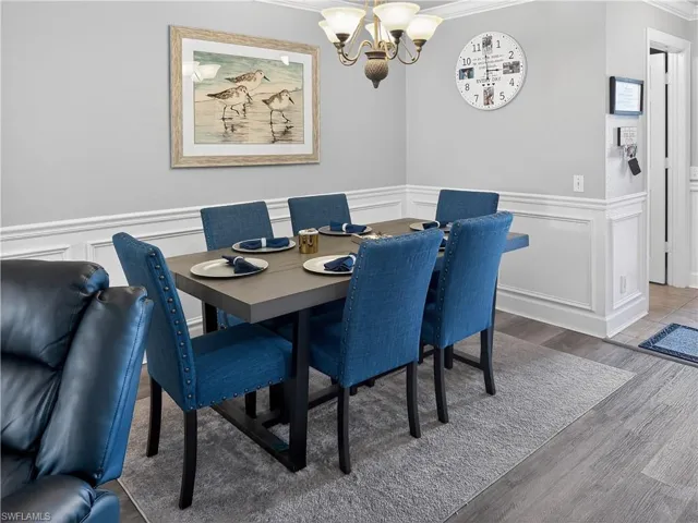 Dining area featuring a decorative wall, wainscoting, crown molding, wood finished floors, and a chandelier