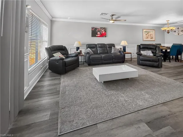 Living room featuring crown molding, a ceiling fan, dark wood finished floors, a decorative wall, and a chandelier