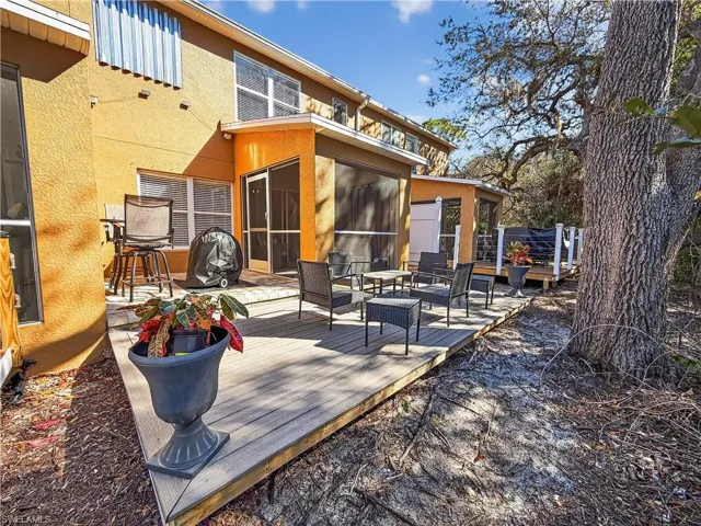 Rear view of property featuring a wooden deck, stucco siding, a sunroom, and an outdoor living space