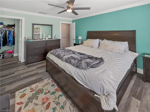 Bedroom featuring dark wood finished floors, ceiling fan, crown molding, and a spacious closet