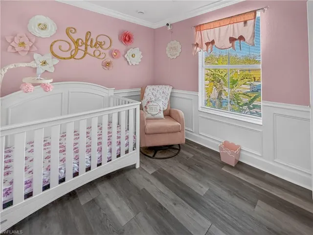 Bedroom with a decorative wall, wainscoting, dark wood finished floors, ornamental molding, and a nursery area