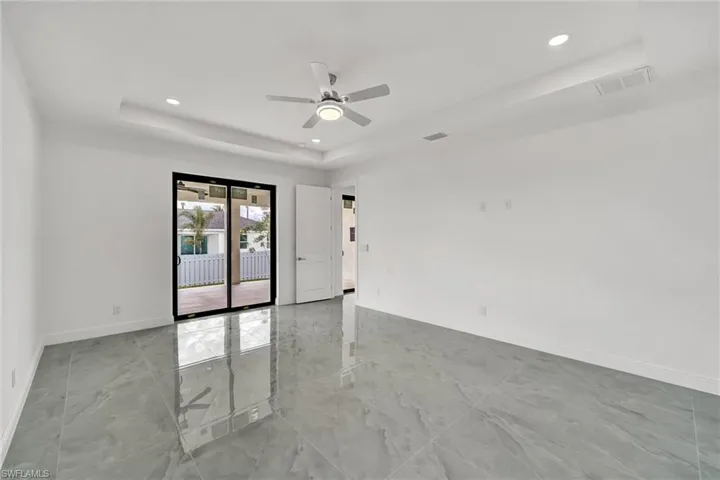 Empty room featuring a tray ceiling, light marble finish flooring, recessed lighting, and a ceiling fan