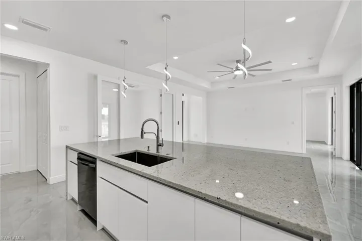 Kitchen featuring dishwashing machine, a ceiling fan, a raised ceiling, white cabinetry, and recessed lighting