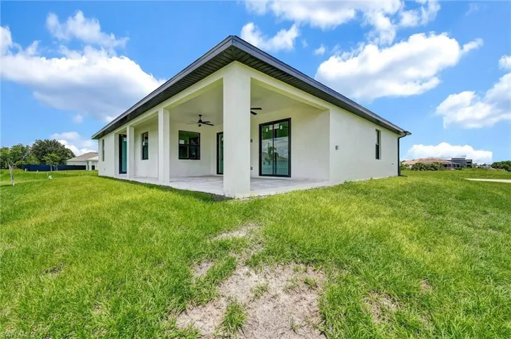 Rear view of property with a ceiling fan, stucco siding, a yard, and a patio