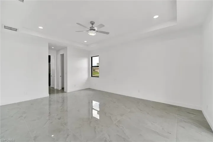 Empty room with a tray ceiling, recessed lighting, light marble finish floors, and ceiling fan