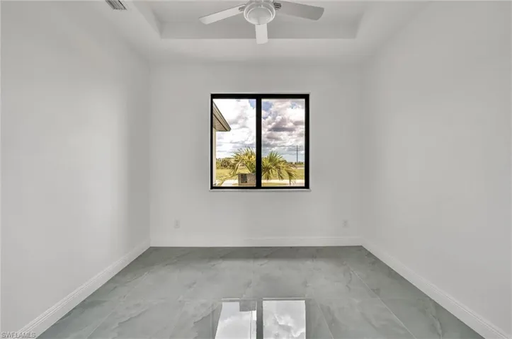 Unfurnished room featuring a raised ceiling, a ceiling fan, and light marble finish flooring