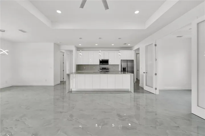 Kitchen with appliances with stainless steel finishes, white cabinetry, recessed lighting, a raised ceiling, and a large island with sink
