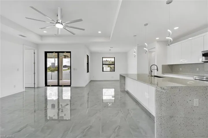 Kitchen with modern cabinets, open floor plan, white cabinets, light stone counters, and recessed lighting