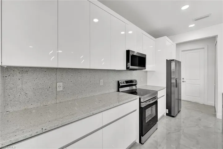 Kitchen with stainless steel appliances, modern cabinets, white cabinetry, light stone countertops, and backsplash