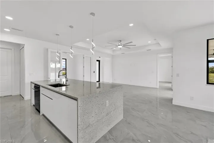 Kitchen with a raised ceiling, an island with sink, white cabinets, light marble finish flooring, and recessed lighting