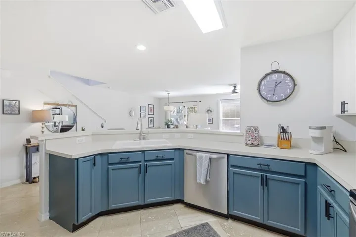Two tone kitchen featuring stainless steel dishwasher, light countertops, two tone cabinets, a peninsula, and decorative light fixtures