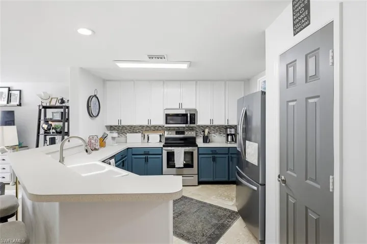 Two tone kitchen featuring a peninsula, stainless steel appliances, light countertops, two tone cabinets, and a breakfast bar area