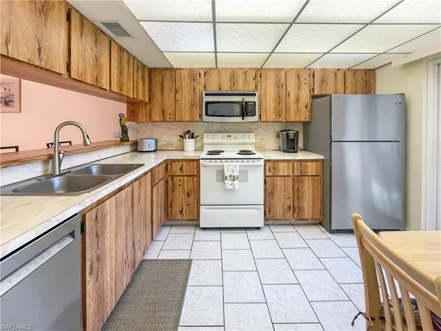 Kitchen featuring stainless steel appliances, light countertops, wood finish cabinets, and a drop ceiling