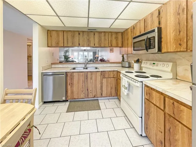 Kitchen featuring stainless steel appliances, a paneled ceiling, light countertops, wood finish cabinetry, and a peninsula