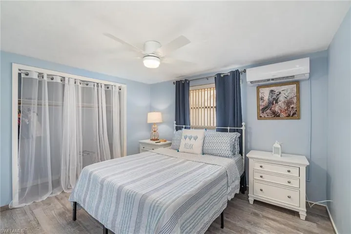 Bedroom with ceiling fan, wood-type flooring, and a wall mounted air conditioner
