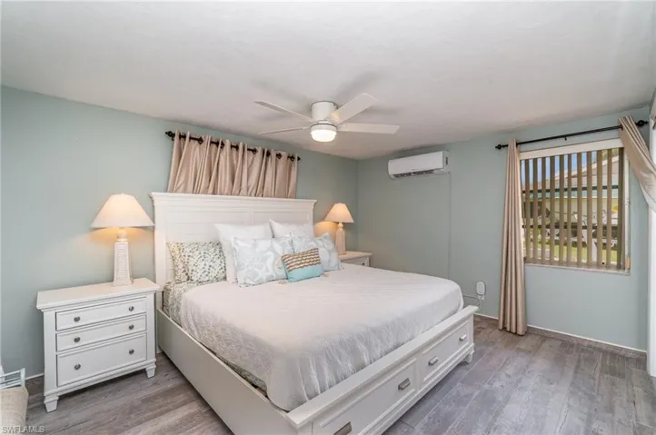 Bedroom featuring a wall mounted air conditioner, wood-type flooring, and ceiling fan