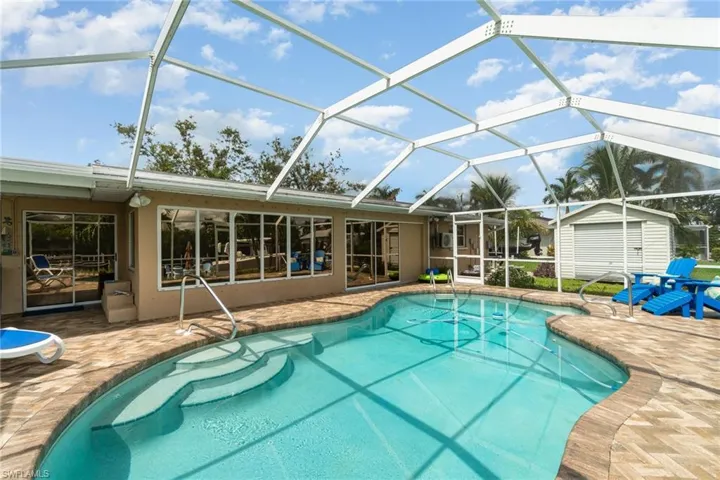 View of pool with a patio area, a storage unit, and glass enclosure