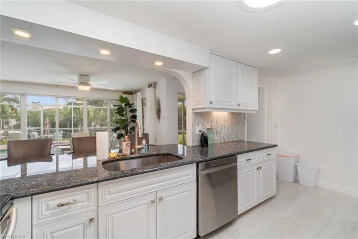 Kitchen with sink, dishwasher, white cabinetry, and dark stone counters