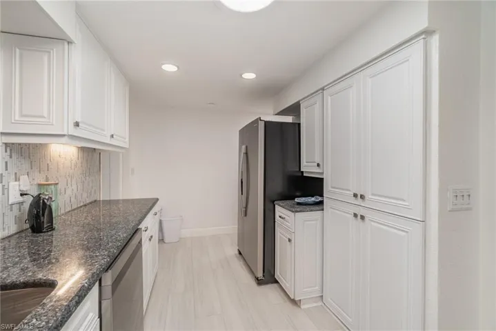 Kitchen featuring stainless steel appliances, decorative backsplash, dark stone counters, and white cabinets
