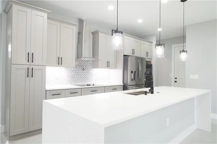 Kitchen with hanging light fixtures, a kitchen island with sink, and stainless steel refrigerator with ice dispenser