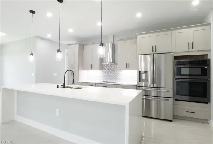 Kitchen featuring hanging light fixtures, stainless steel appliances, sink, wall chimney exhaust hood, and tasteful backsplash