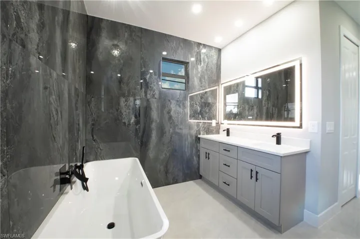 Bathroom with tile patterned flooring, a tub, vanity, and tile walls